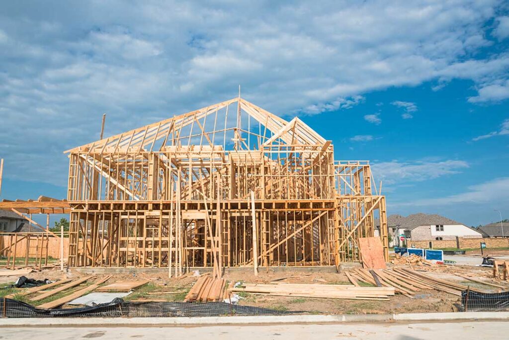 Architects discussing blueprints outdoors on a construction site with the sun behind a partially constructed commercial building.