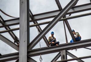 A maintenance worker inspects rooftop solar panels on a commercial office building under a partly cloudy sky.