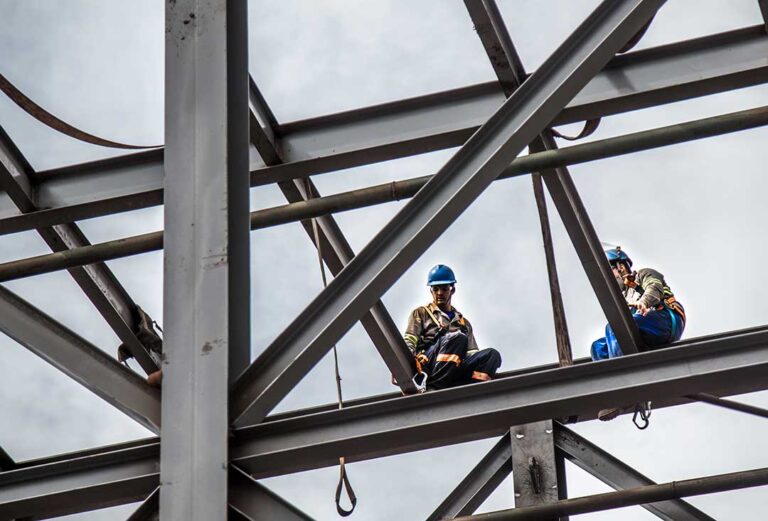 A maintenance worker inspects rooftop solar panels on a commercial office building under a partly cloudy sky.