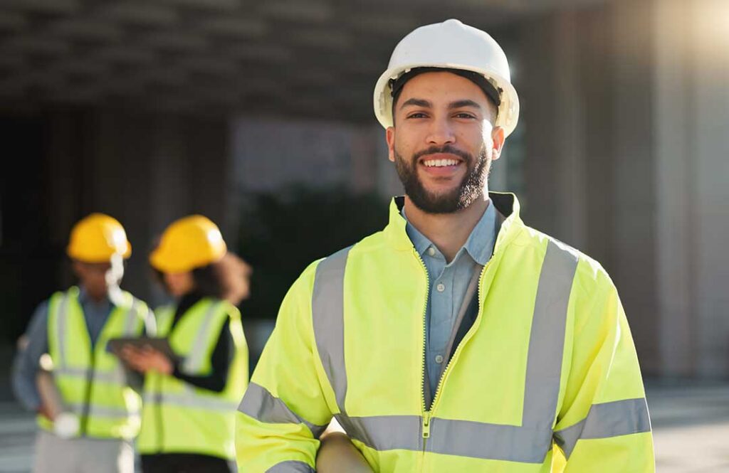 Construction workers reviewing building plans at an active job site with structural framing visible in the background.